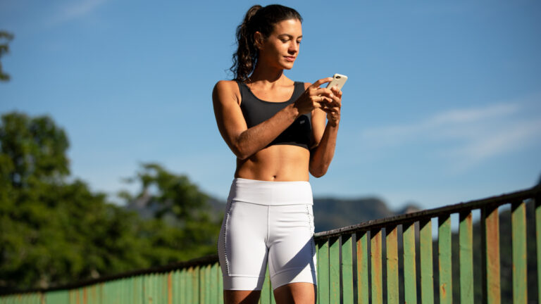 mulher-vendo-celular-vestindo-linha-grit-authen-ar-livre | Blog 10 coisas que você precisa saber para iniciar 2021 com o pé direito na corrida