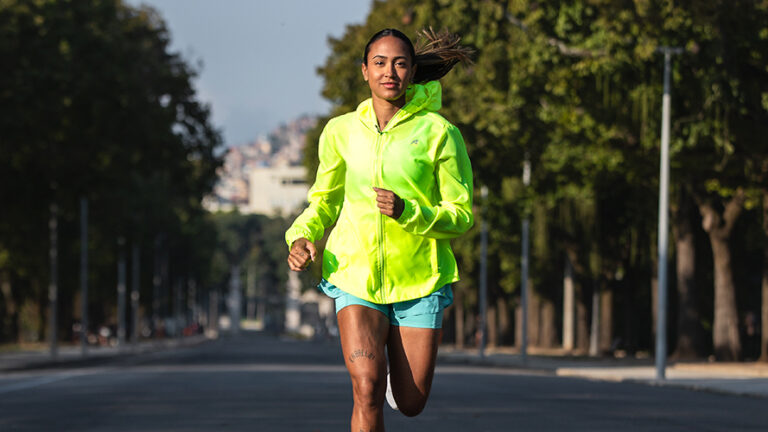 Mulher correndo em uma estrada com roupa adequada para o frio, vestindo um casaco amarelo e shorts. Ideal para praticar atividades físicas em baixas temperaturas.