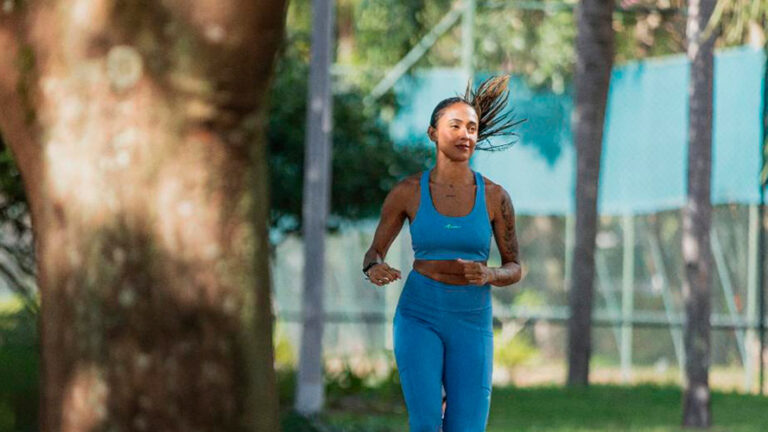 Mulher praticando corrida ao ar livre em diferentes zonas de treino. Cercada por árvores e por natureza, ideal para atividades físicas e exercícios em ambientes abertos.