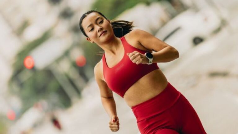 Mulher praticando corrida de rua na cidade, usando roupas esportivas vermelhas e descansando ao longo do percurso